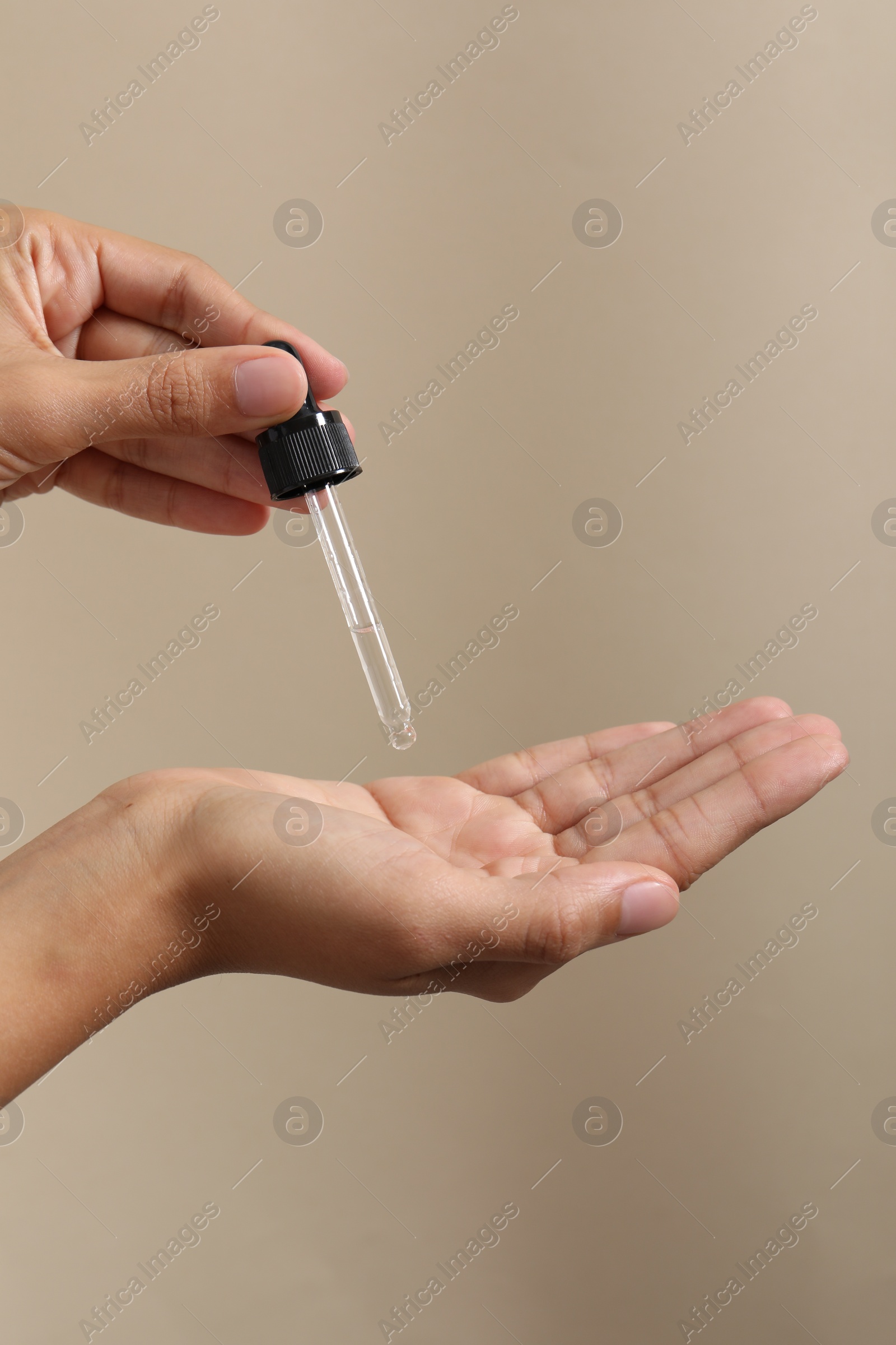 Photo of Woman applying cosmetic serum onto her hand on beige background, closeup