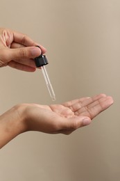 Woman applying cosmetic serum onto her hand on beige background, closeup