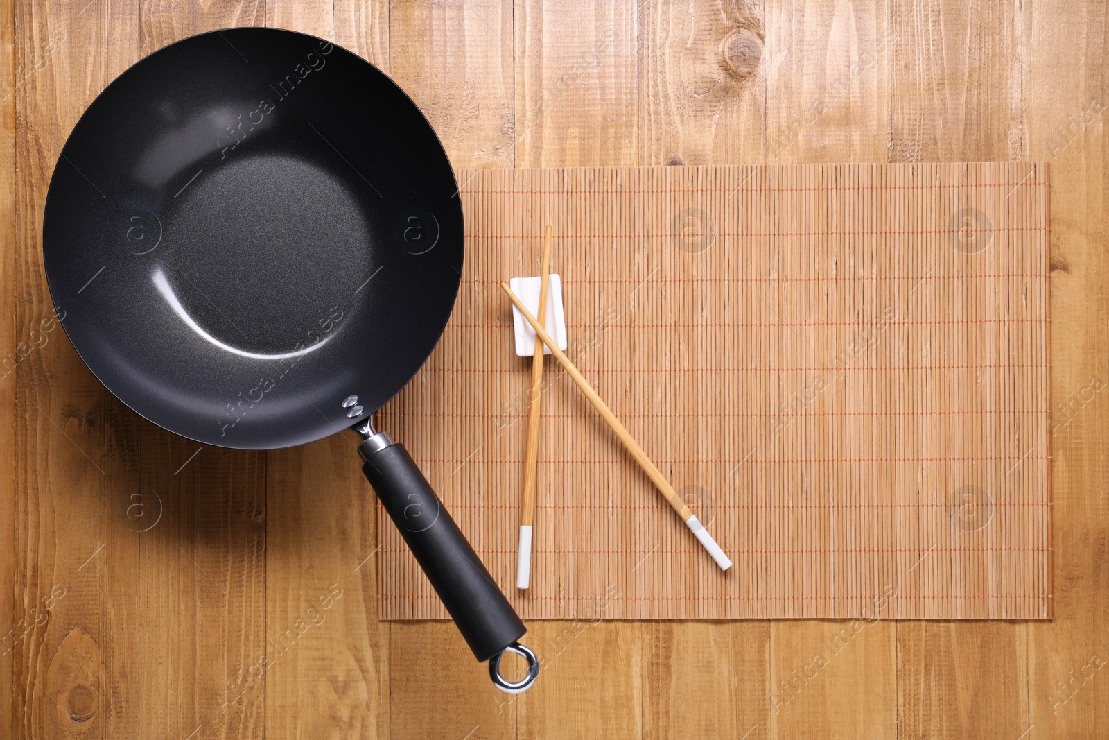 Photo of Empty iron wok and chopsticks on wooden table, top view. Space for text