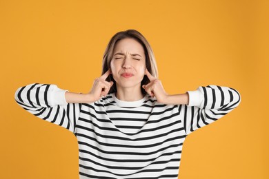 Photo of Emotional young woman covering her ears with fingers on yellow background
