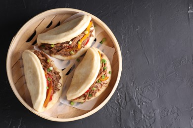 Photo of Delicious gua bao in bamboo steamer on black table, top view. Space for text
