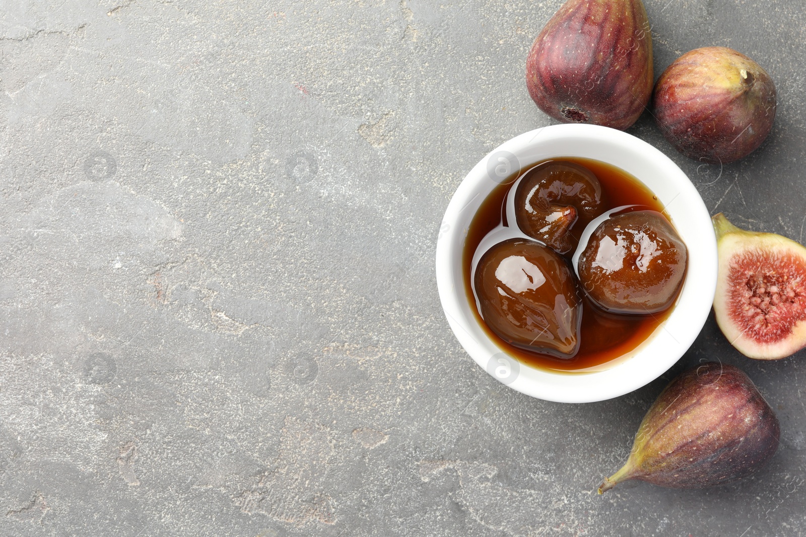 Photo of Bowl of tasty sweet jam and fresh figs on grey table, flat lay. Space for text