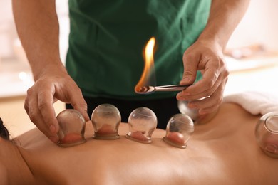 Therapist giving fire cupping treatment to patient indoors, closeup