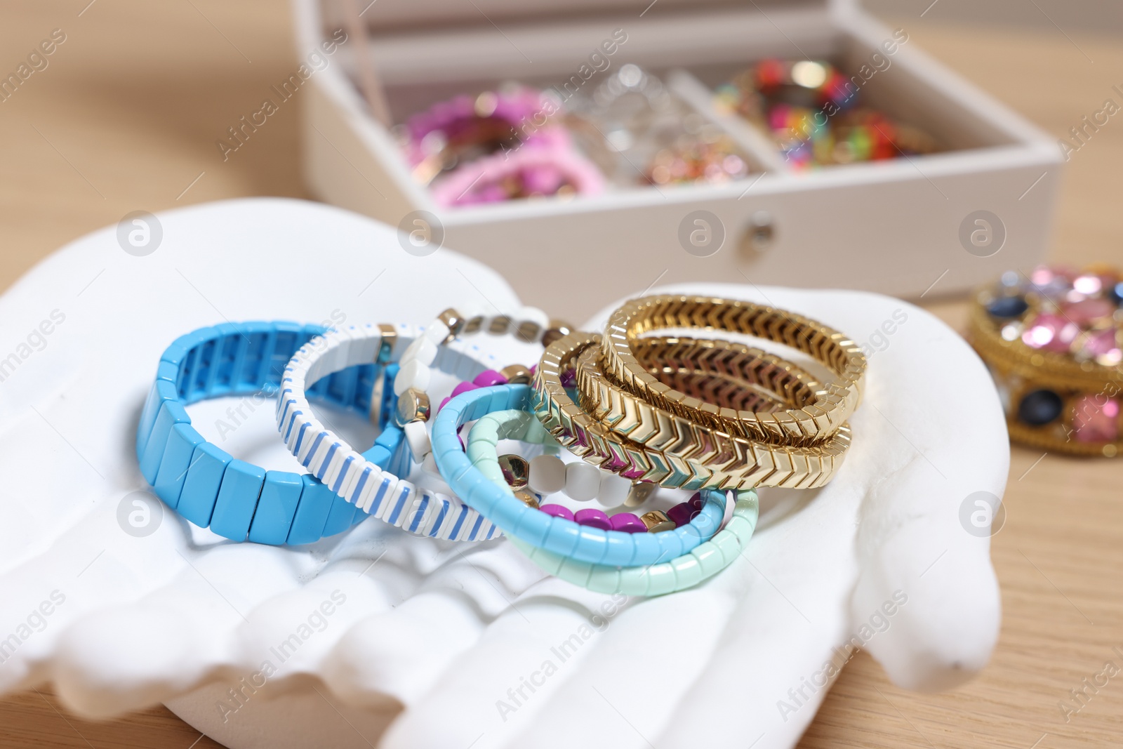 Photo of Ceramic hand stand with many different bracelets on wooden table, closeup