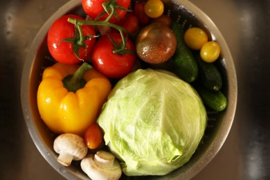 Photo of Different wet vegetables in metal colander inside sink, top view