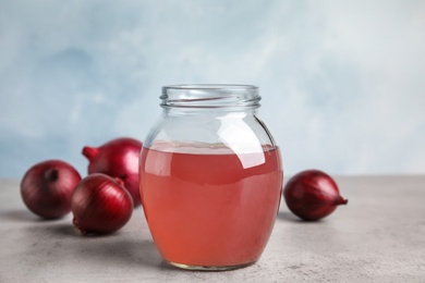 Glass jar of onion syrup and fresh vegetable on table