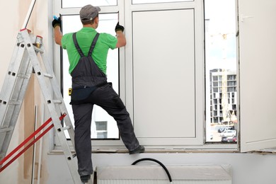 Photo of Worker in uniform installing double glazing window indoors, back view