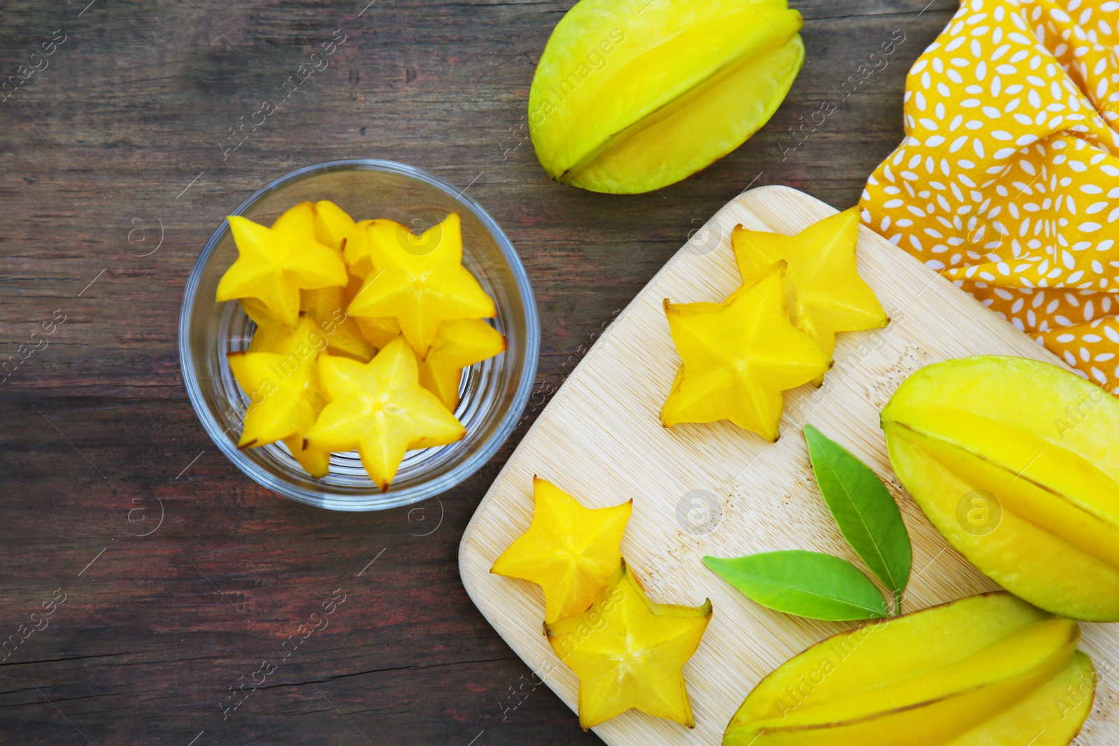 Photo of Delicious cut and whole carambolas with green leaves on wooden table, flat lay