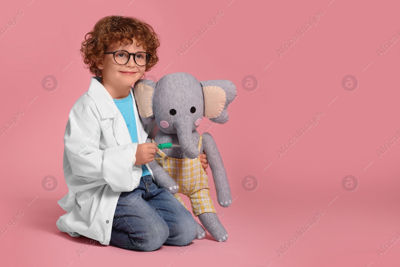 Photo of Little boy in medical uniform with thermometer and toy elephant on pink background. Space for text