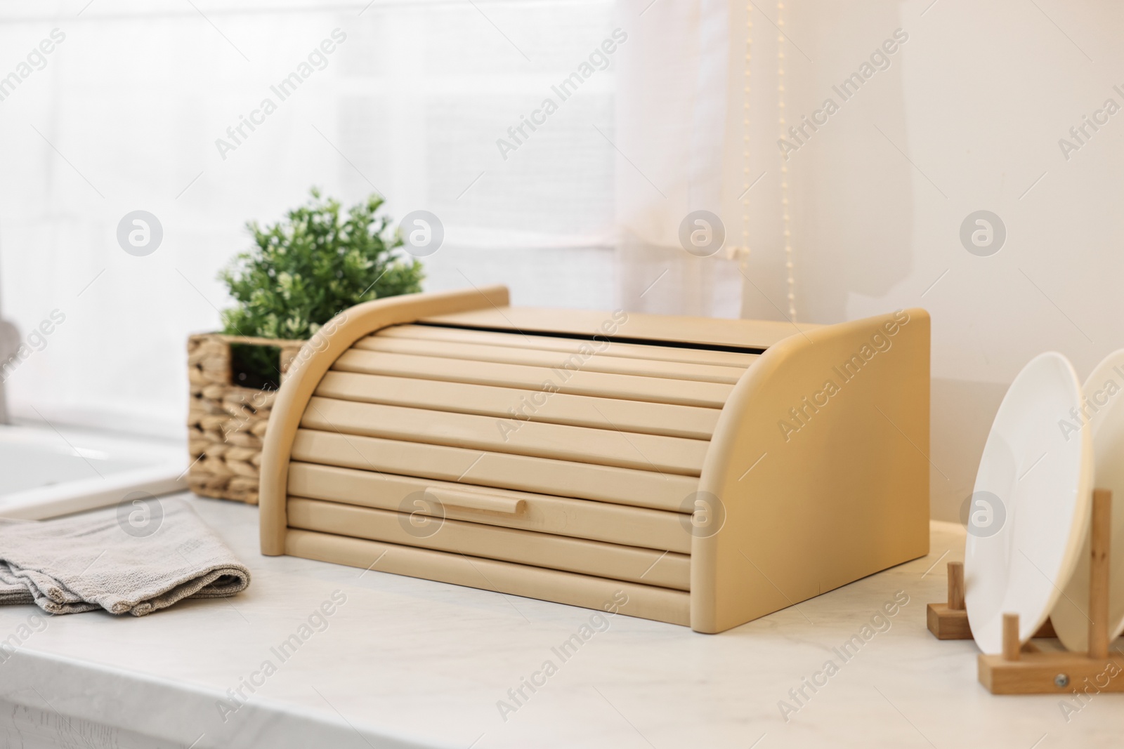 Photo of Wooden bread box, houseplant and plates on white marble countertop in kitchen