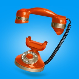 Image of Vintage orange corded telephone flying in air on light blue background