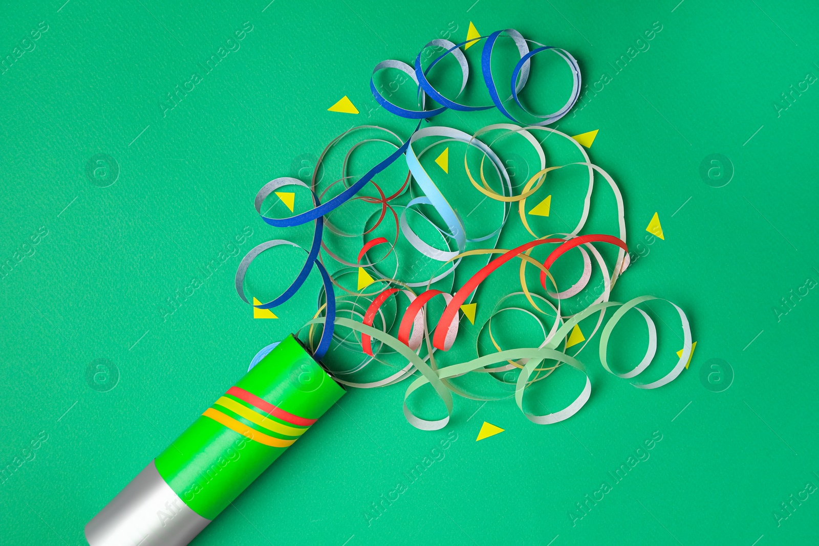 Photo of Beautiful serpentine and confetti bursting out of party popper on green background, flat lay