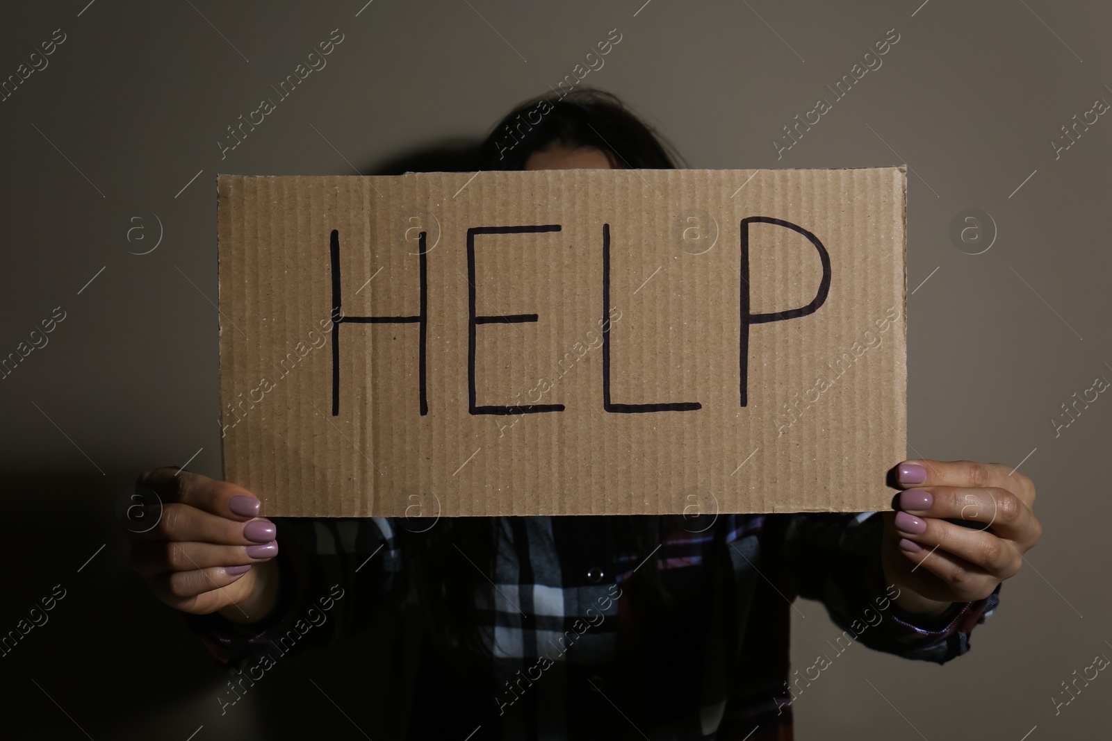 Photo of Young woman with sign HELP near beige wall. Domestic violence concept