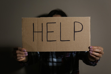 Photo of Young woman with sign HELP near beige wall. Domestic violence concept