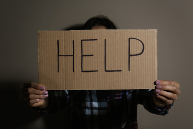 Young woman with sign HELP near beige wall. Domestic violence concept