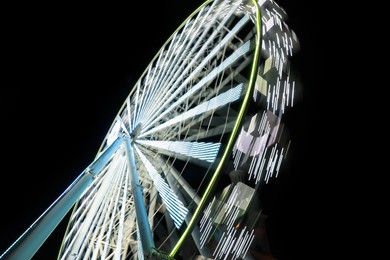 Photo of Beautiful glowing Ferris wheel against dark sky, motion blur effect