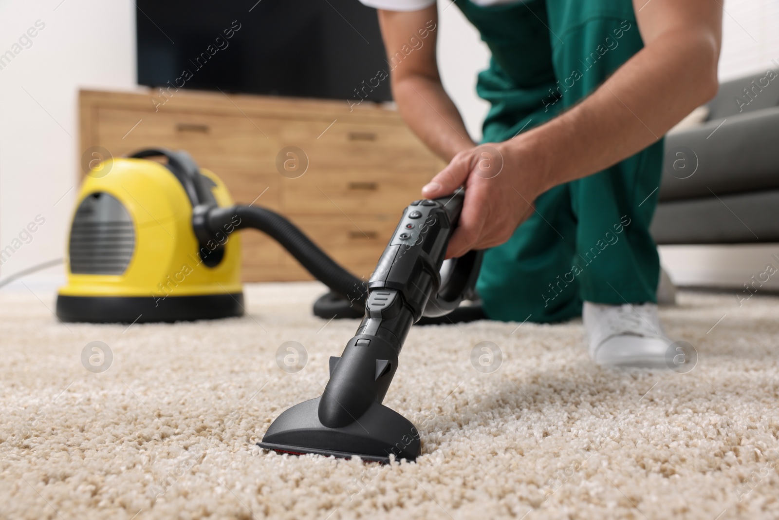 Photo of Dry cleaner's employee hoovering carpet with vacuum cleaner indoors, closeup