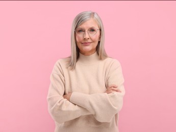 Photo of Portrait of beautiful middle aged woman in eyeglasses with crossed arms on pink background