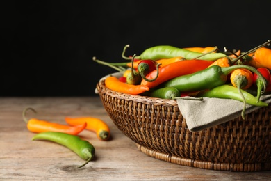 Photo of Wicker bowl with different chili peppers on wooden table, closeup. Space for text