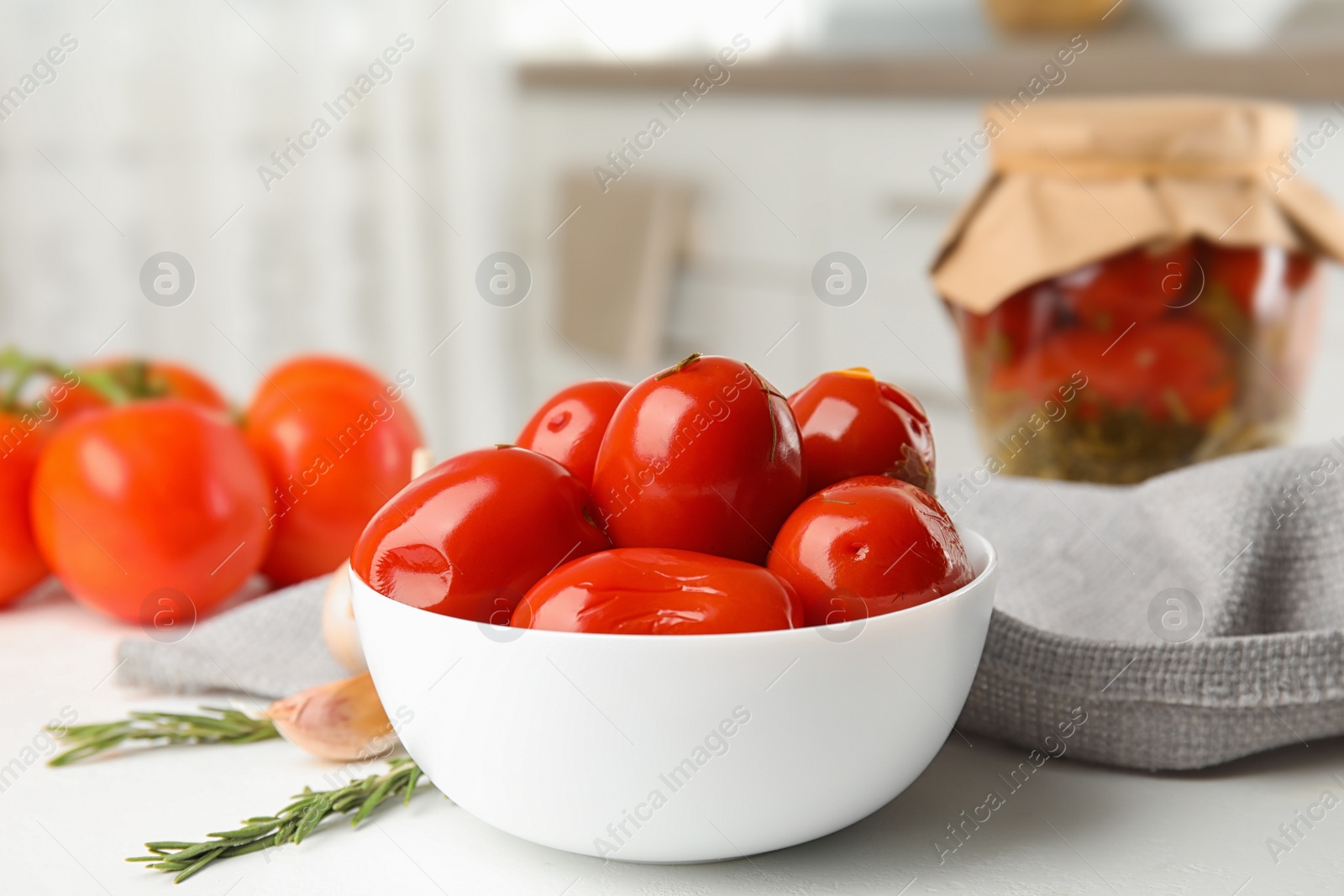 Photo of Pickled tomatoes in bowl near glass jar on white kitchen table