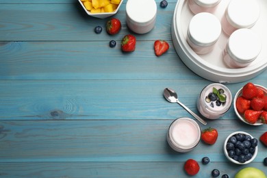 Modern yogurt maker with full jars and different fruits on light blue wooden table, flat lay. Space for text