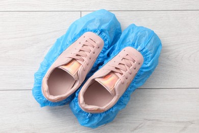 Women`s sneakers in blue shoe covers on light wooden floor, top view