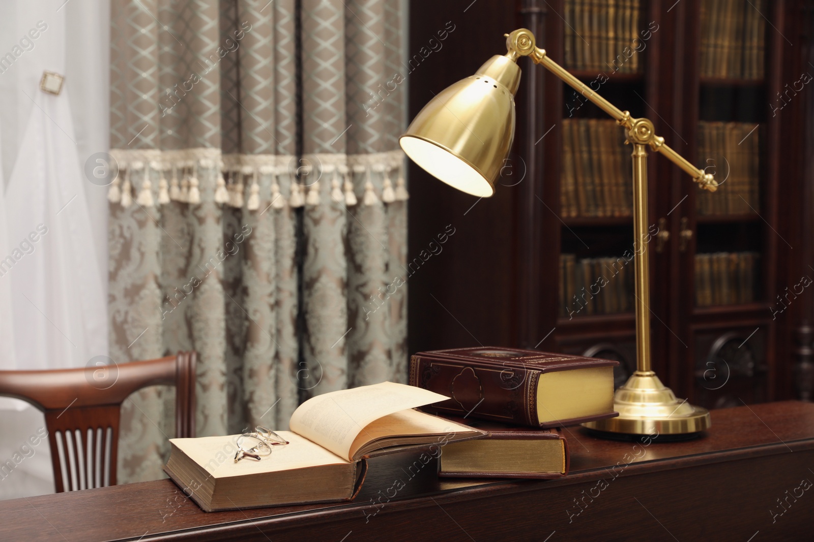 Photo of Books, glasses and lamp on wooden table in library reading room