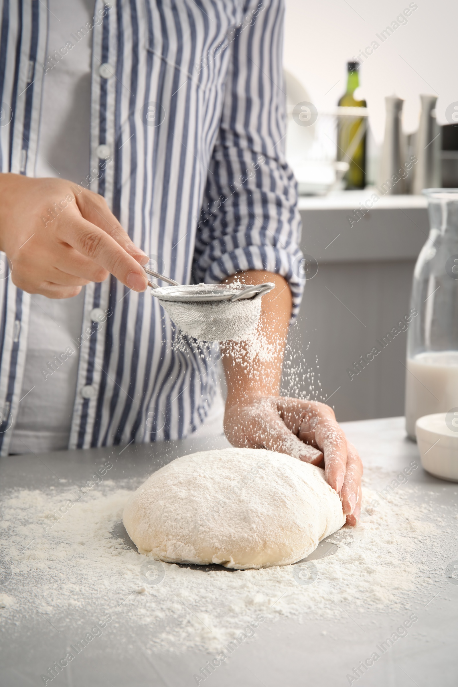 Photo of Woman sprinkling dough for pastry with flour on table