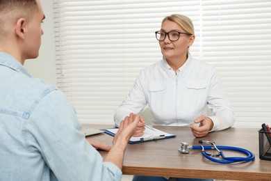 Photo of Professional doctor having discussion with patient at wooden table in clinic