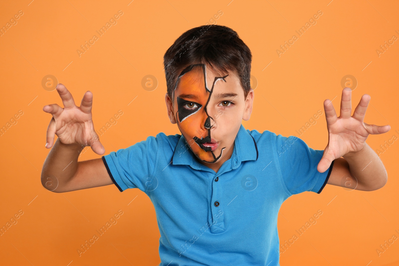 Photo of Cute little boy with face painting on orange background