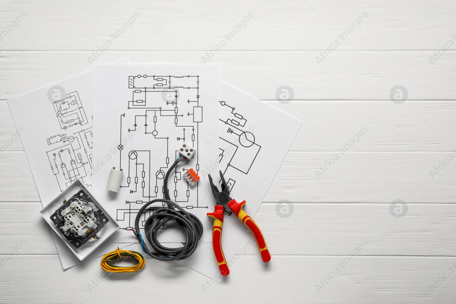 Photo of Wiring diagrams, wires, pliers and disassembled light switch on white wooden table, top view. Space for text