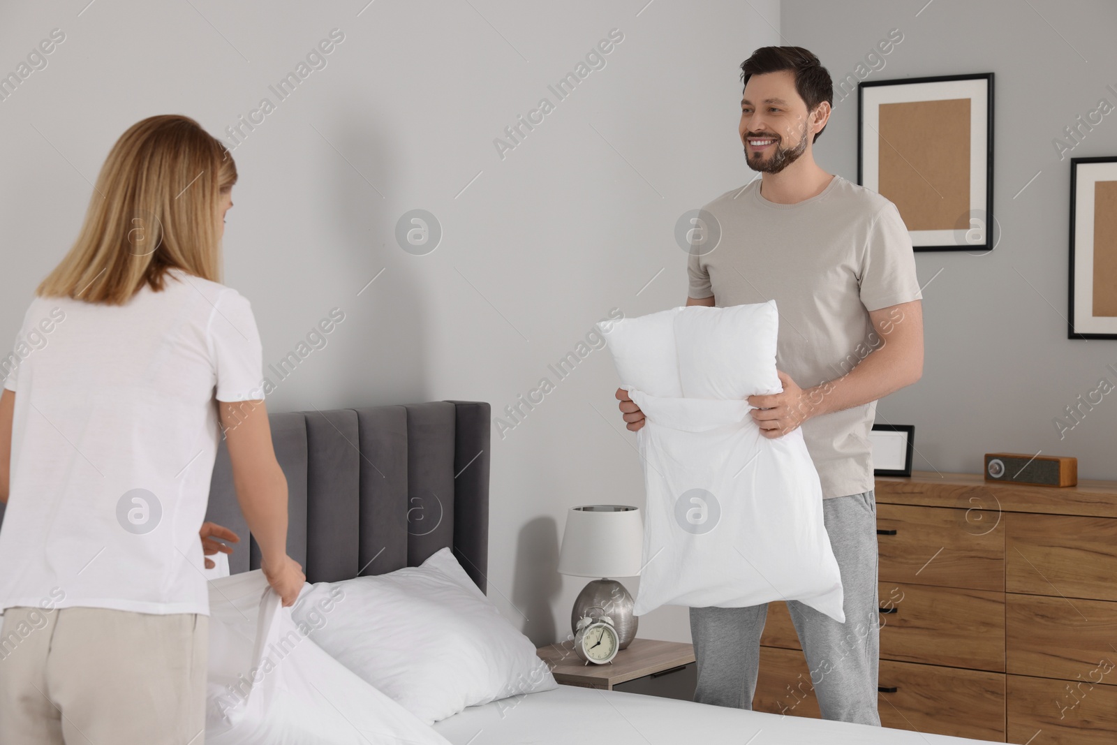 Photo of Couple changing bed linens in room. Domestic chores