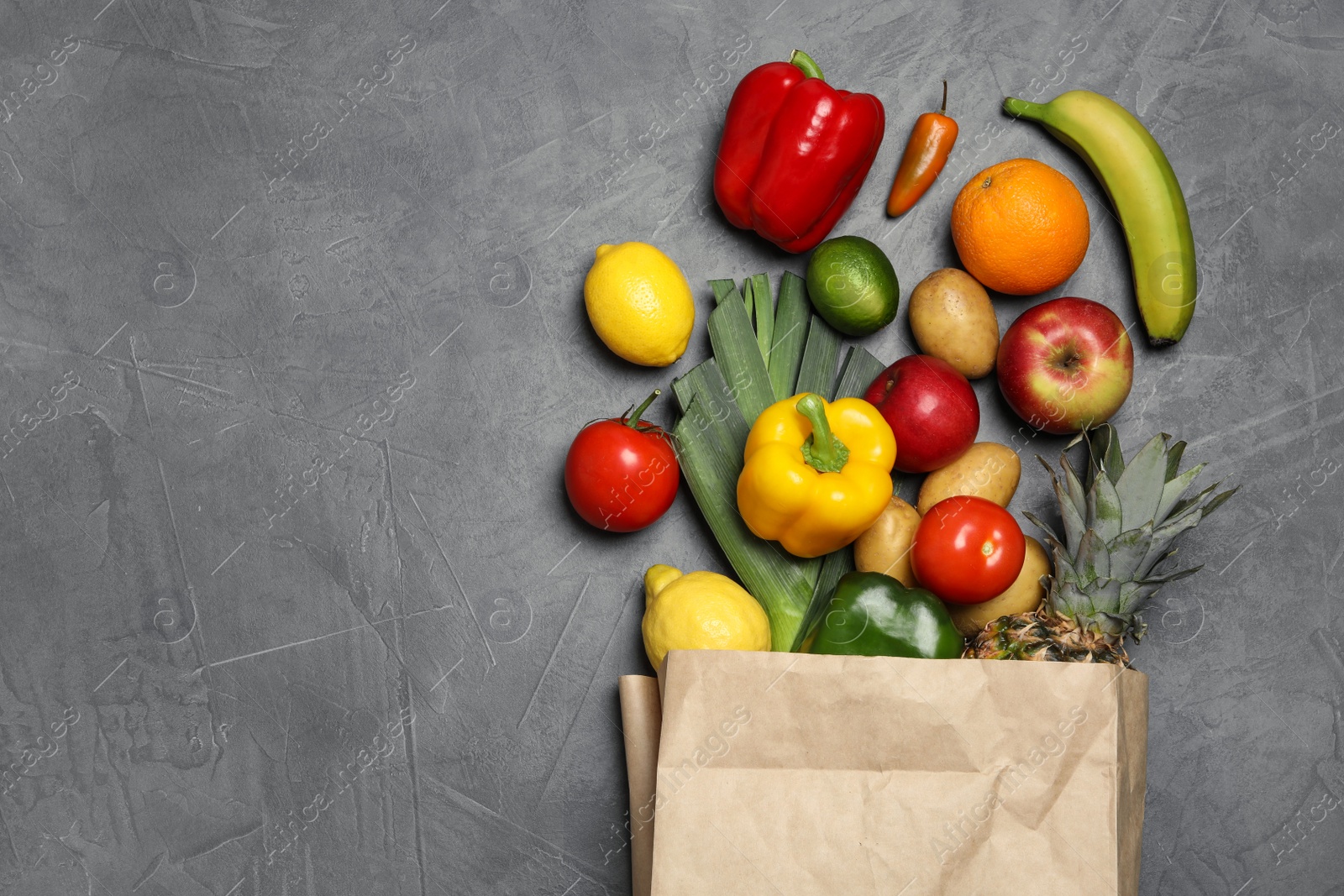 Photo of Paper bag with fresh vegetables and fruits on grey background, flat lay. Space for text