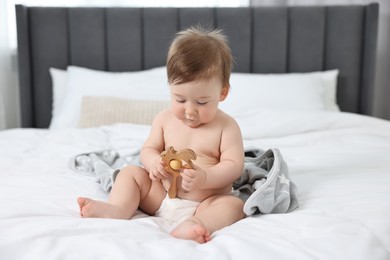Cute baby boy with blanket and rattle sitting on bed at home
