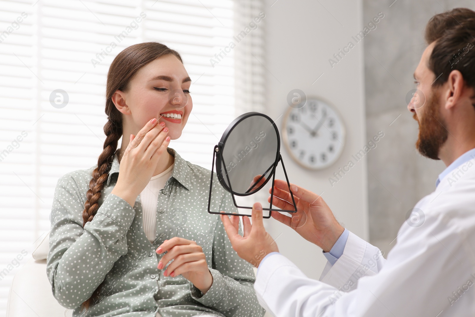 Photo of Young woman looking at her new dental implants in mirror indoors