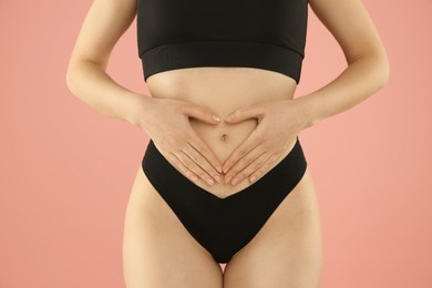 Photo of Gynecology. Woman in underwear making heart with her hands on pink background, closeup