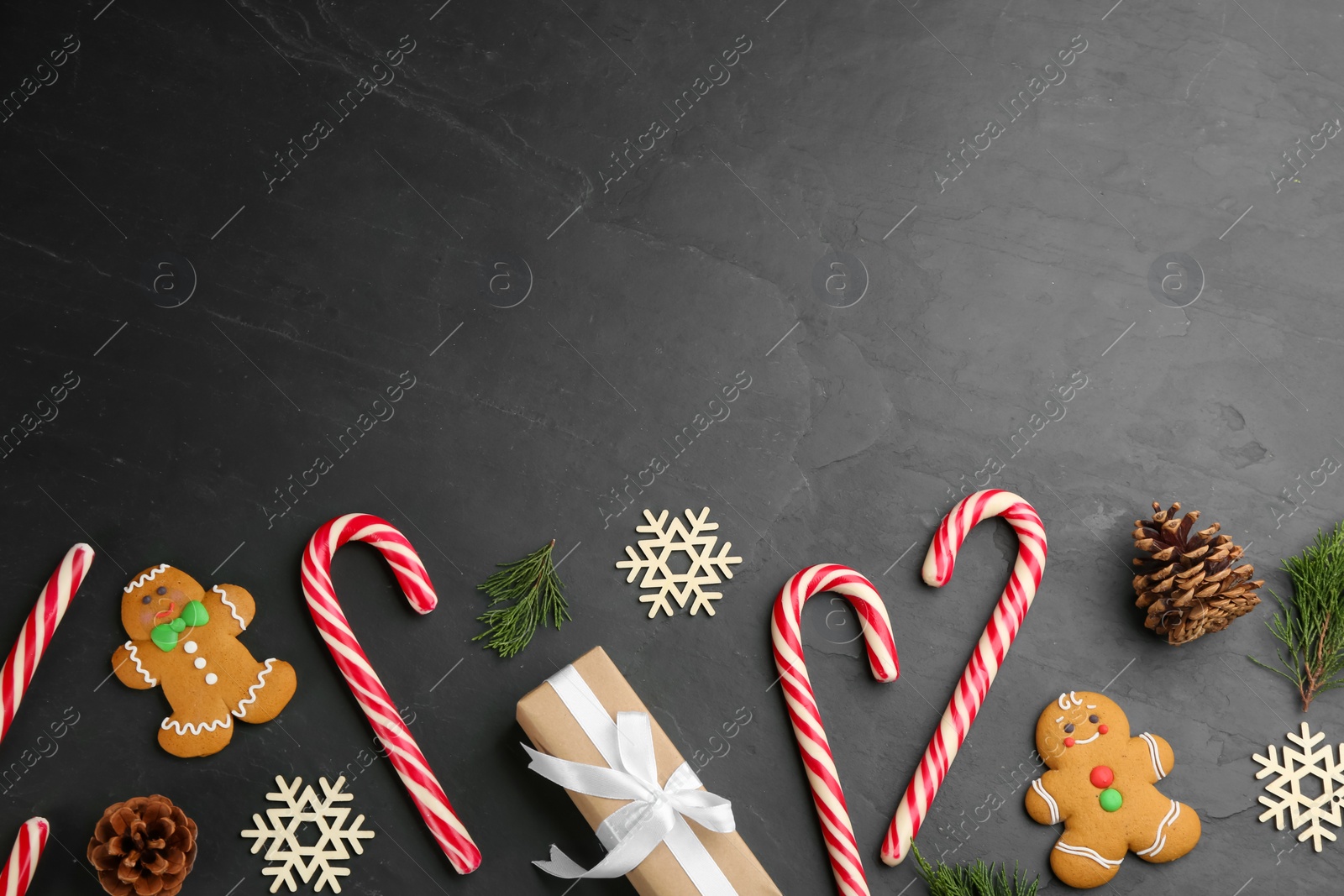 Photo of Flat lay composition with candy canes and Christmas decor on black table. Space for text