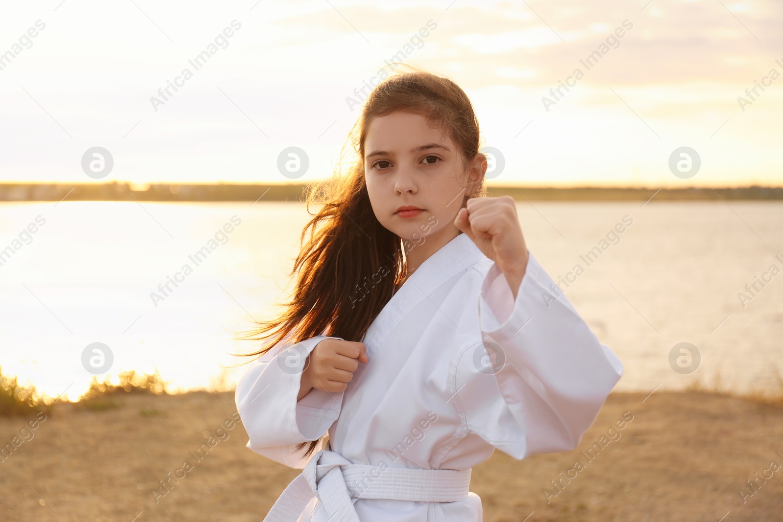 Photo of Cute little girl in kimono practicing karate near river at sunset