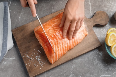 Photo of Woman cutting raw salmon fillet on wooden board, top view