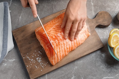 Woman cutting raw salmon fillet on wooden board, top view