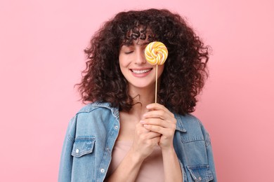 Beautiful woman covering eye with lollipop on pink background