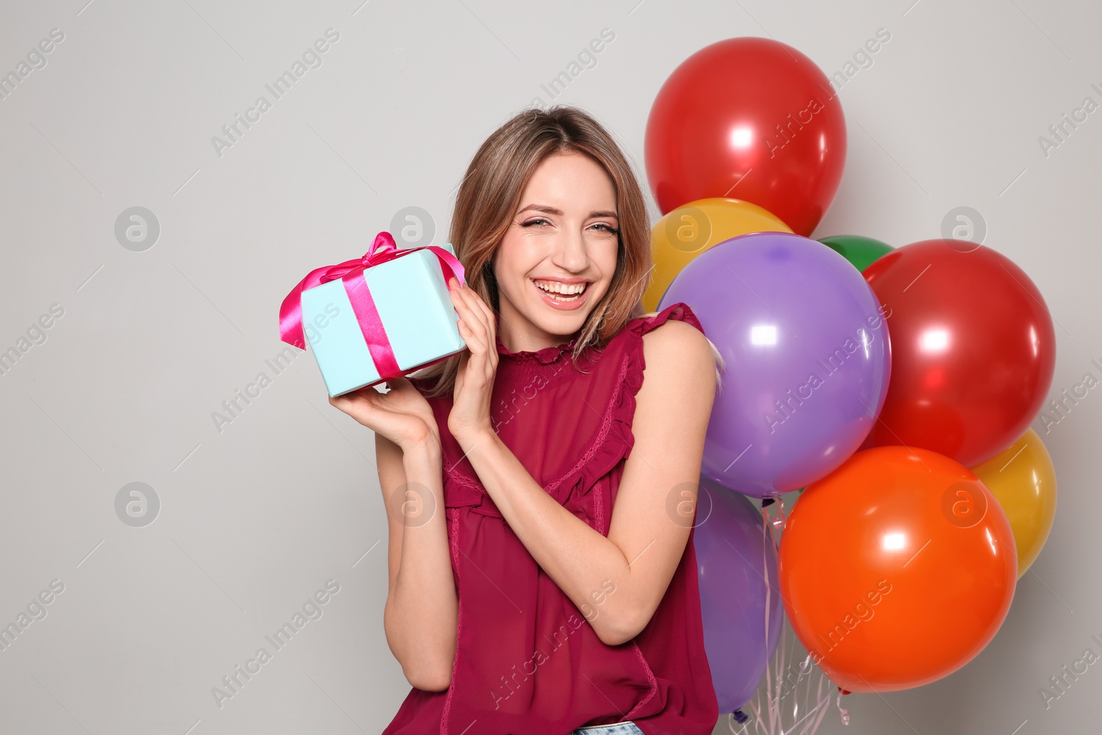 Photo of Portrait of beautiful smiling girl with gift box and air balloons on light background. International Women's Day