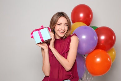 Portrait of beautiful smiling girl with gift box and air balloons on light background. International Women's Day