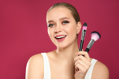 Photo of Beautiful woman with makeup brushes on pink background