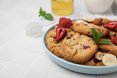 Photo of Cookies with freeze dried fruits, mint and nuts on white tiled table, closeup. Space for text