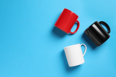 Photo of Colorful ceramic mugs on light blue background, flat lay. Space for text