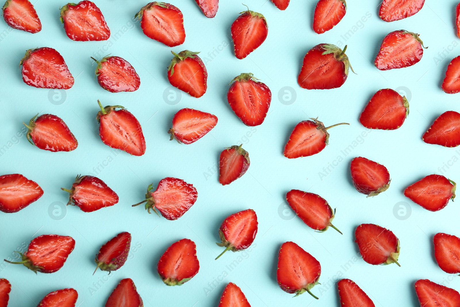 Photo of Halves of delicious ripe strawberries on light blue background, flat lay