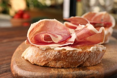 Board of tasty sandwiches with cured ham and cream cheese on wooden table, closeup
