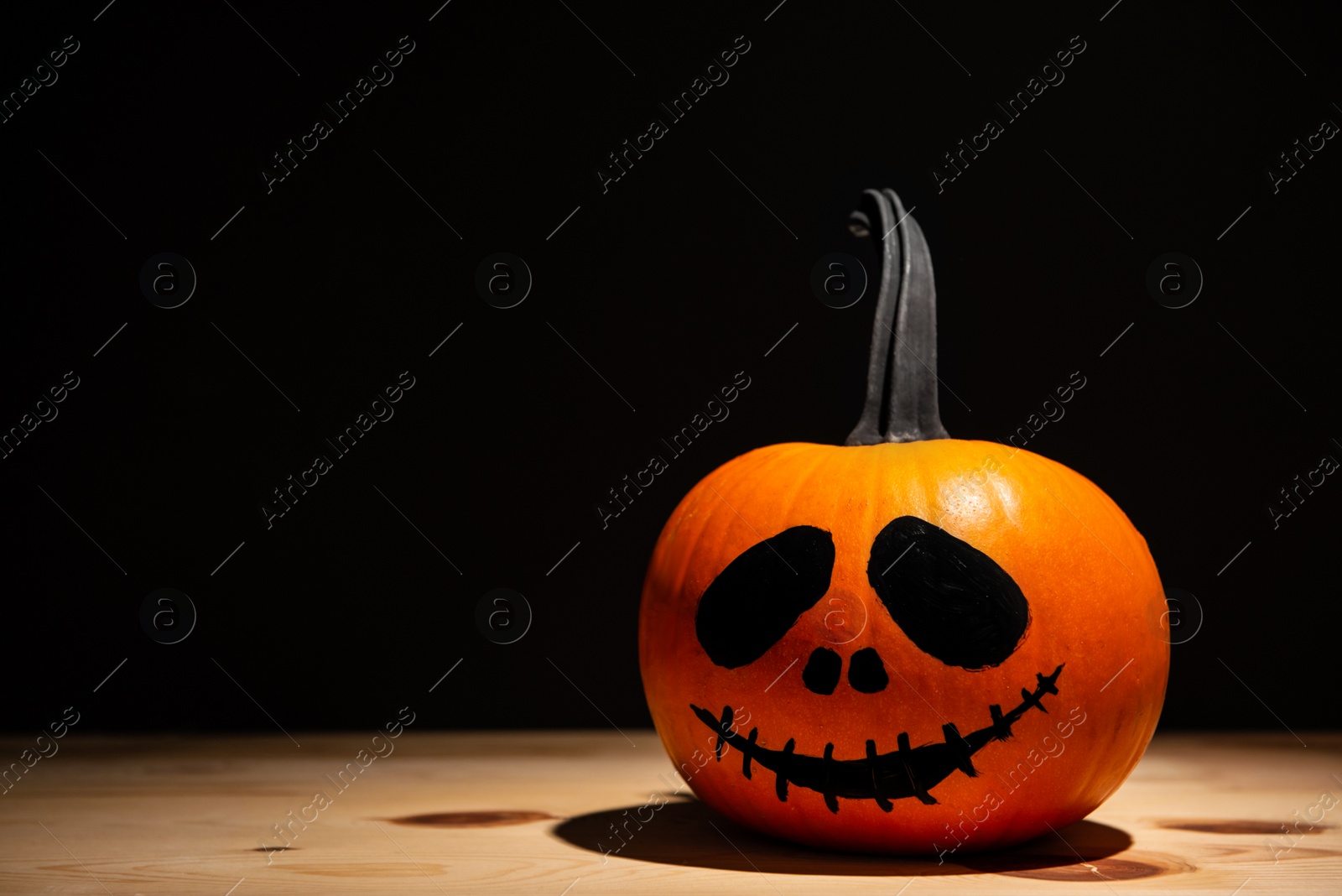 Photo of Halloween celebration. Pumpkin with drawn face on wooden table against black background, space for text