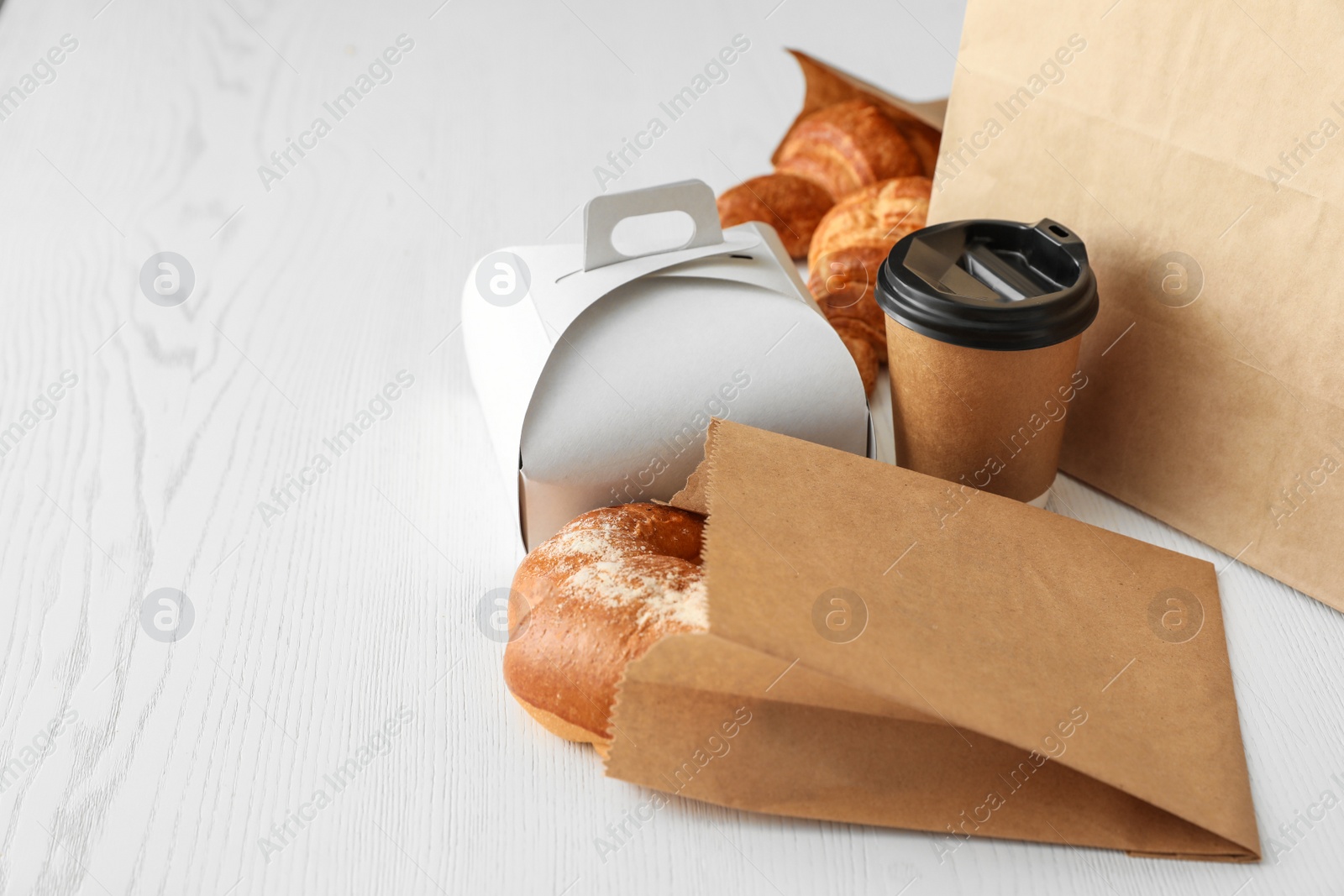 Photo of Paper bag with pastry and takeaway food on wooden table. Space for text